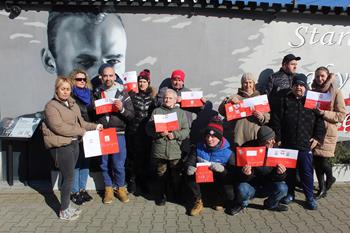 Uczestnicy oraz kadra ŚDS w Gryfinie stoją przed muralem Rotmistrza Witolda Pileckiego trzymając flagi